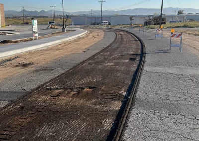 A road under construction with barriers and a section of asphalt removed, under a clear blue sky.