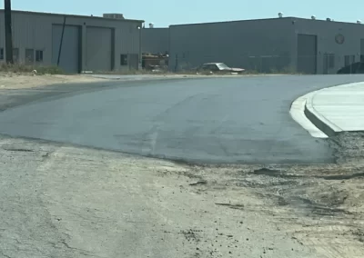 A newly paved road curves past industrial buildings under a clear blue sky.