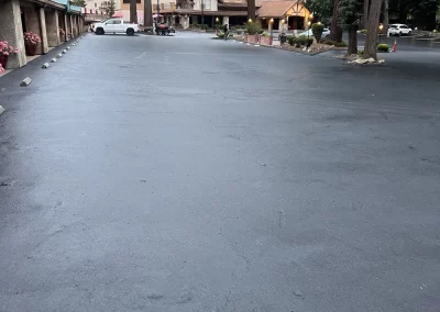 Freshly paved parking lot in front of a rustic lodge surrounded by tall trees and parked cars.