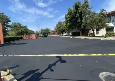 Freshly paved street blocked by yellow caution tape under a blue sky with scattered clouds.