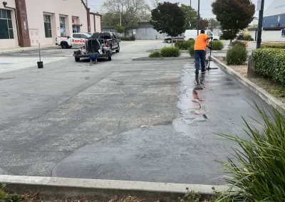 A worker in an orange vest sprays water on a wet parking lot near a Jack in the Box restaurant.
