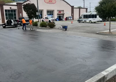 Two workers in a parking lot near an Ace Hardware store with fresh pavement on a cloudy day.