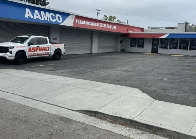 AAMCO auto shop with a white Asphalt truck parked outside on a cloudy day.