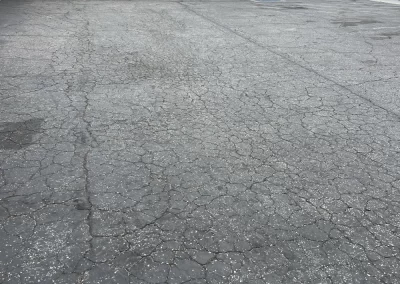 A cracked, empty parking lot in front of a white building with red and blue trim.