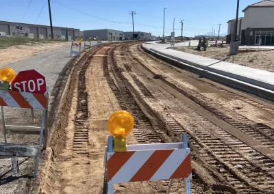 A construction zone with dirt road, barriers, stop sign, and tire tracks under a clear blue sky.