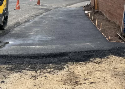 Freshly paved driveway next to a wooden fence, with construction cones and equipment nearby.
