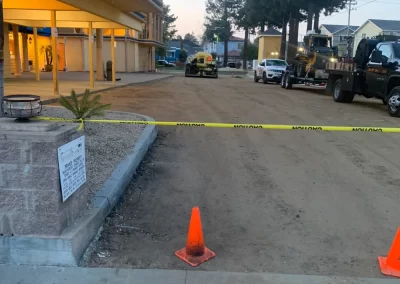 A dirt road under construction, blocked by caution tape and orange cones near a building entrance.
