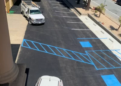 View of a newly paved parking lot with fresh blue-striped handicap parking spaces and several parked vehicles.