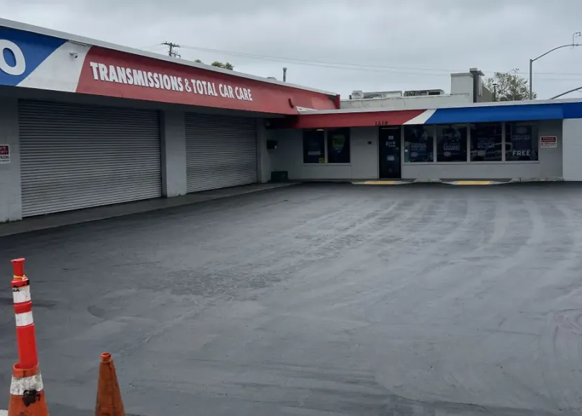 Auto repair shop with closed garage doors, empty parking lot, and an orange traffic cone in front.